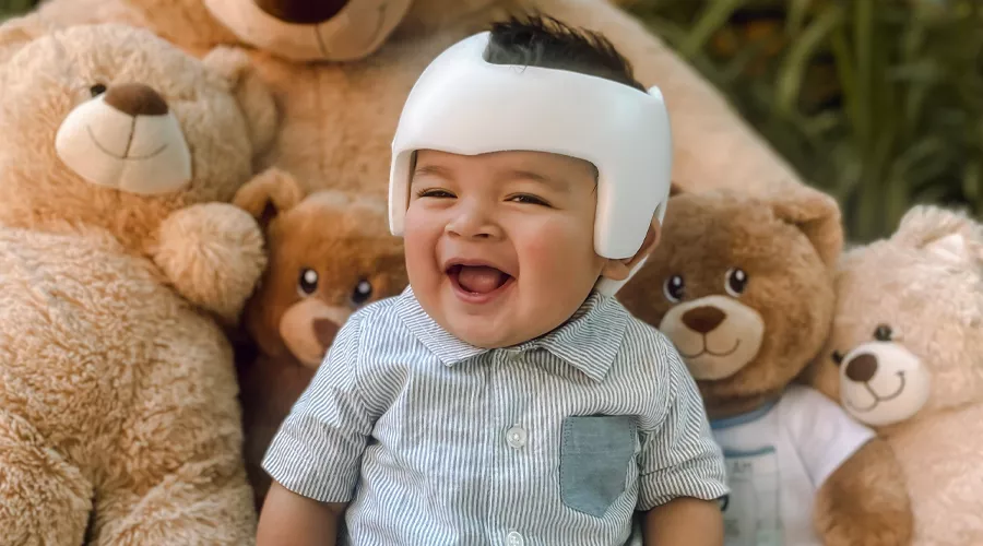 Baby boy in doc band smiling next to teddy bears